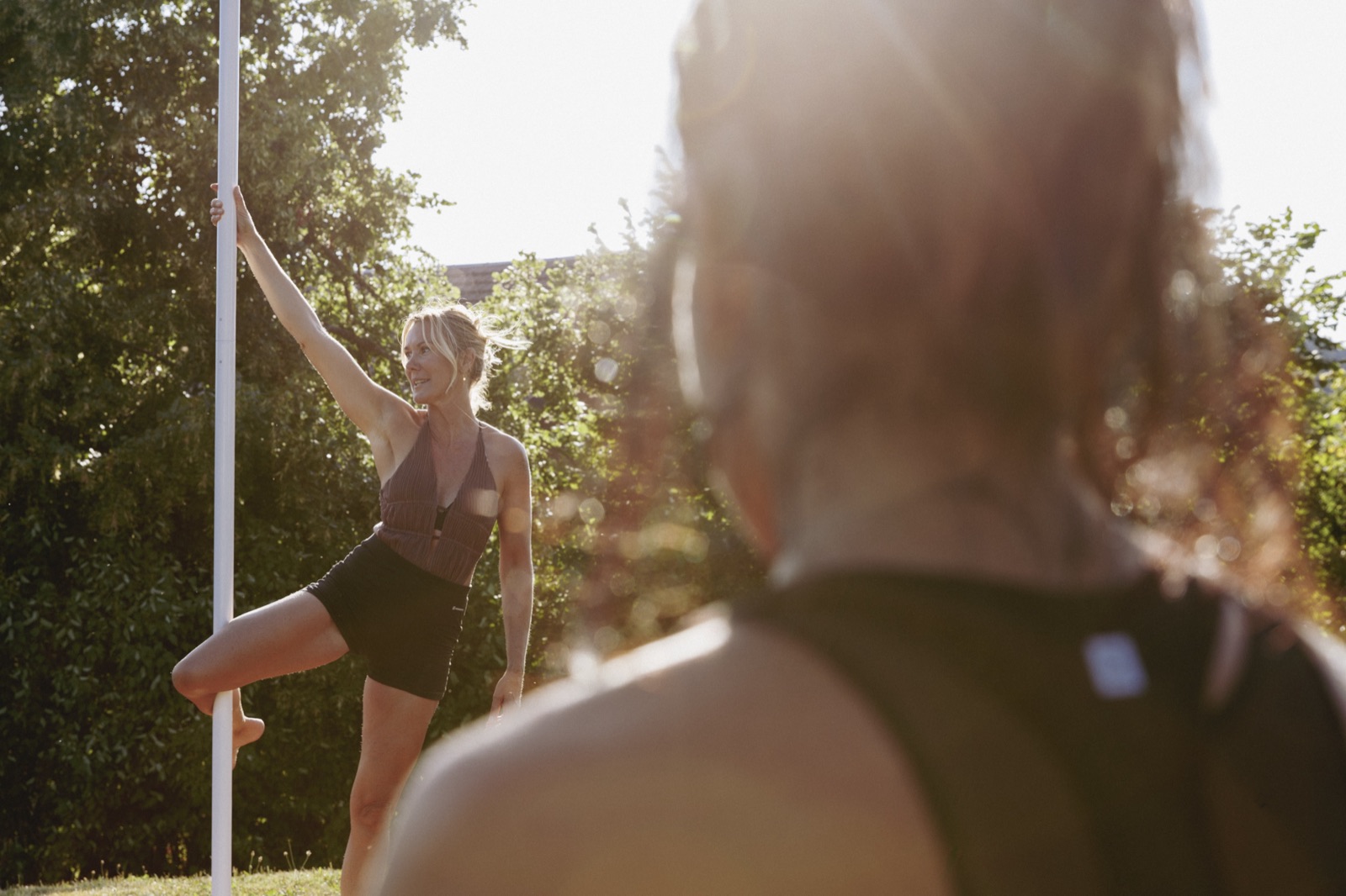 Professeure de pole dance montrant une figure simple à la barre, en extérieur