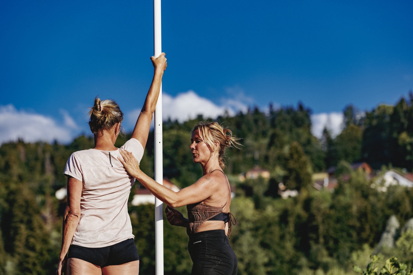 Professeure accompagnant une élève à la barre lors d'un cours de pole dance en extérieur
